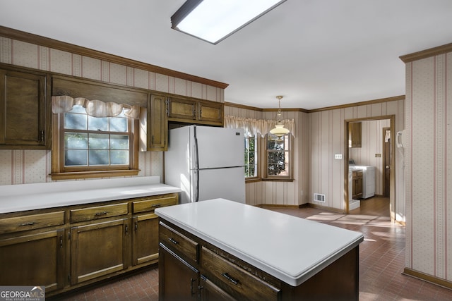 kitchen with light countertops, hanging light fixtures, freestanding refrigerator, washer / clothes dryer, and wallpapered walls