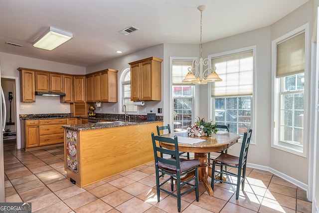 kitchen with pendant lighting, sink, light tile patterned floors, dark stone countertops, and a notable chandelier