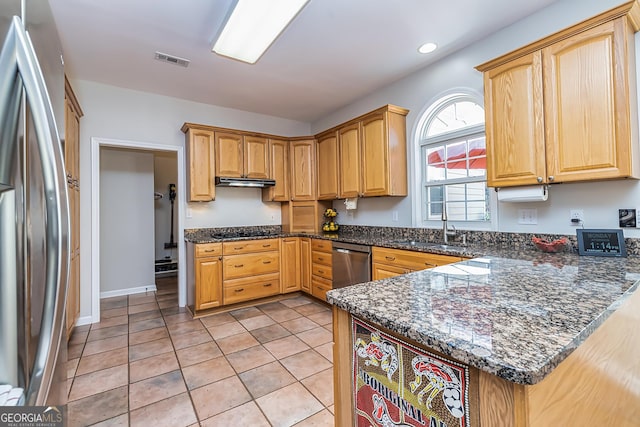 kitchen with sink, light tile patterned floors, appliances with stainless steel finishes, kitchen peninsula, and dark stone counters