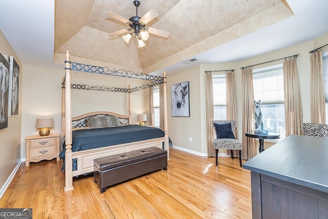 bedroom with lofted ceiling, light hardwood / wood-style flooring, a raised ceiling, and ceiling fan