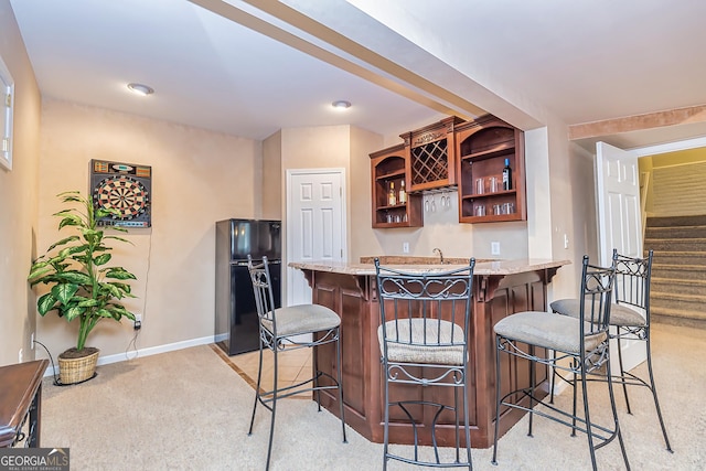 kitchen with light stone countertops, black refrigerator, light carpet, and a kitchen bar