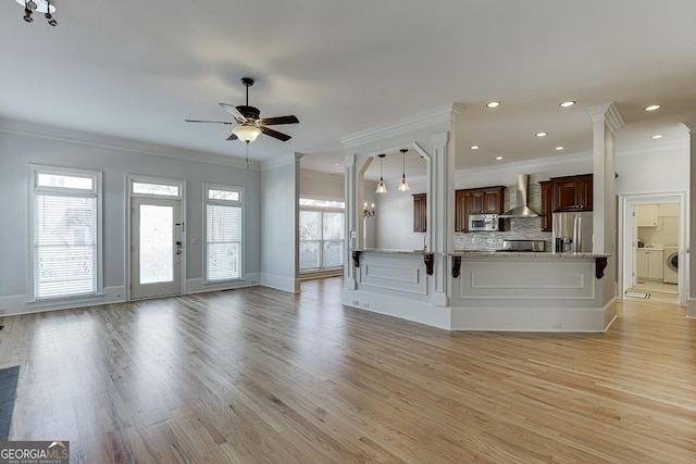 unfurnished living room with ornamental molding, washer / dryer, ceiling fan with notable chandelier, and light hardwood / wood-style floors