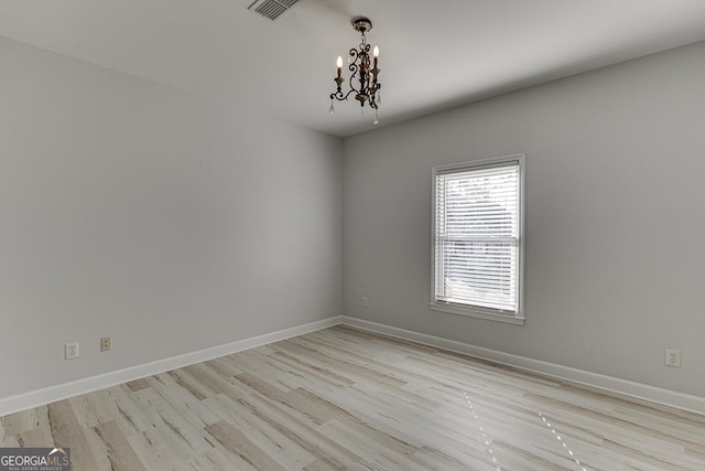 empty room featuring light hardwood / wood-style flooring and a notable chandelier