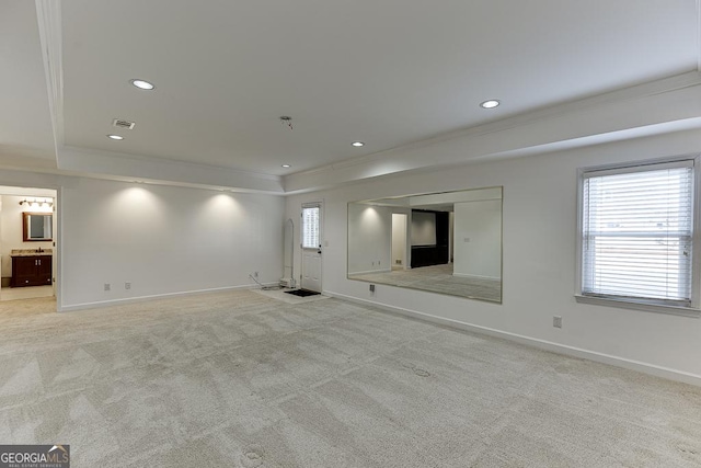 unfurnished living room with light colored carpet, ornamental molding, and a tray ceiling