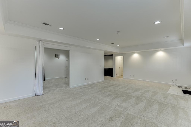 spare room with crown molding, a tray ceiling, and light colored carpet