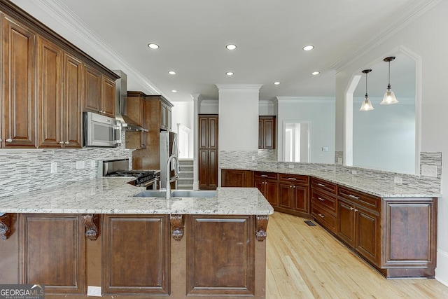 kitchen featuring appliances with stainless steel finishes, sink, light stone counters, kitchen peninsula, and wall chimney range hood