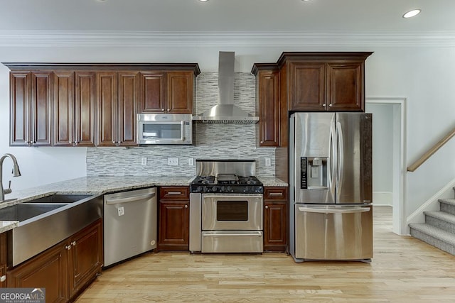 kitchen with wall chimney exhaust hood, light hardwood / wood-style flooring, ornamental molding, stainless steel appliances, and light stone countertops