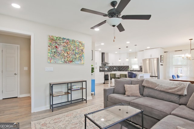 living room featuring sink, ceiling fan with notable chandelier, and light hardwood / wood-style floors