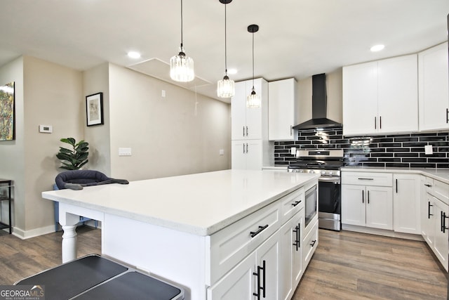 kitchen featuring wall chimney exhaust hood, white cabinetry, decorative light fixtures, appliances with stainless steel finishes, and backsplash