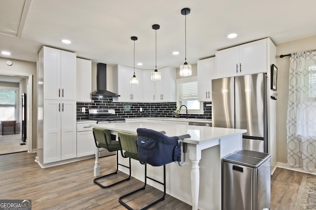 kitchen featuring white cabinetry, a center island, wall chimney exhaust hood, and appliances with stainless steel finishes