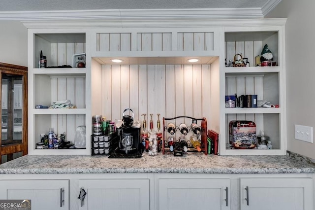 kitchen featuring light stone counters, built in shelves, crown molding, and white cabinetry