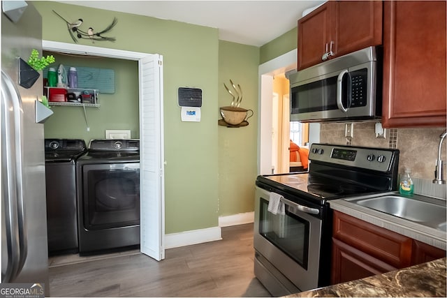 kitchen with sink, wood-type flooring, stainless steel appliances, washer and clothes dryer, and decorative backsplash