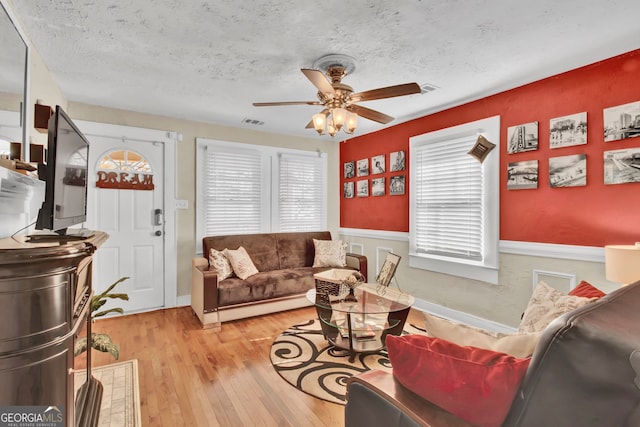 living room featuring ceiling fan, light hardwood / wood-style floors, and a textured ceiling