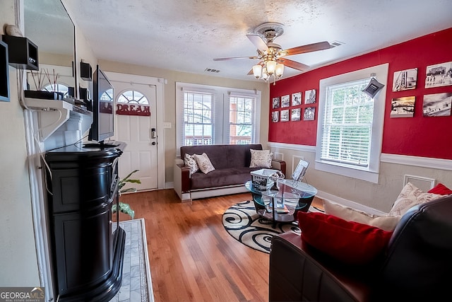 living room with ceiling fan, a textured ceiling, and light hardwood / wood-style floors