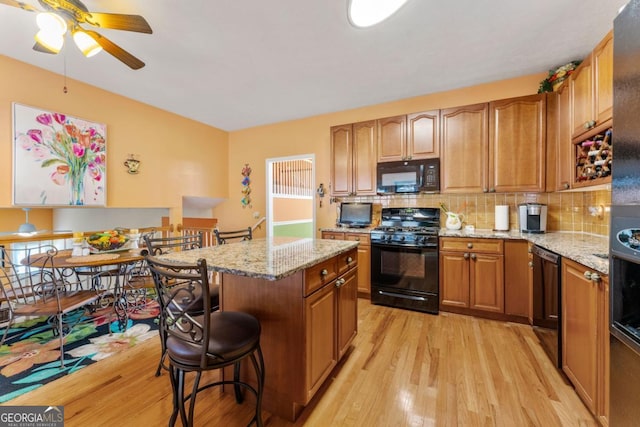 kitchen with backsplash, a center island, black appliances, light stone countertops, and light hardwood / wood-style flooring