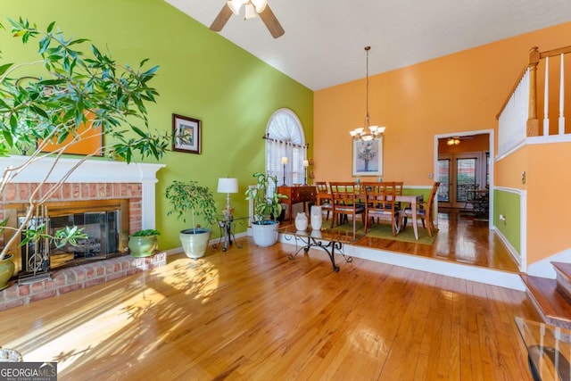 living room featuring hardwood / wood-style flooring, high vaulted ceiling, ceiling fan with notable chandelier, and a fireplace