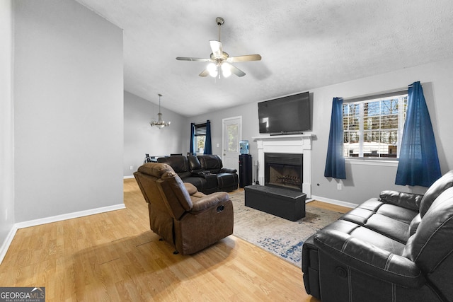 living room with wood-type flooring, lofted ceiling, ceiling fan with notable chandelier, and a textured ceiling