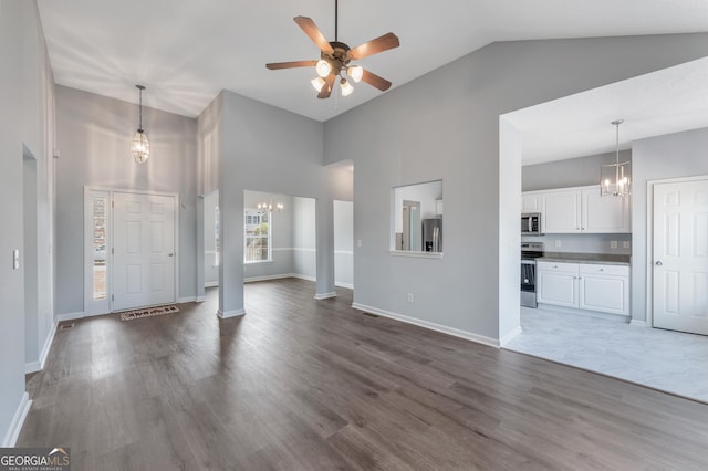 unfurnished living room with hardwood / wood-style flooring, ceiling fan with notable chandelier, and high vaulted ceiling