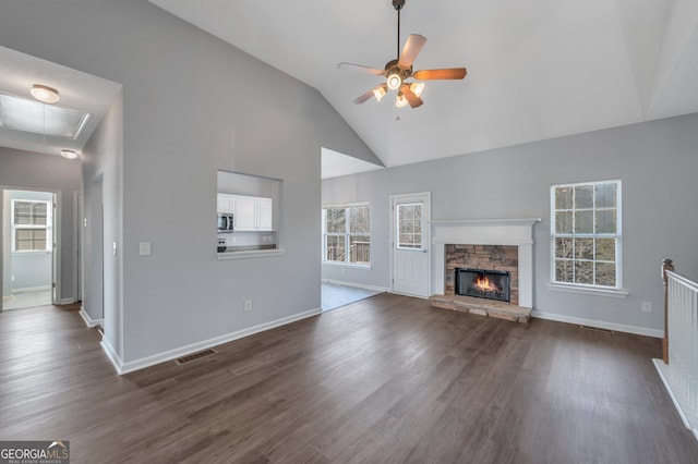 unfurnished living room with a stone fireplace, dark wood-type flooring, high vaulted ceiling, and ceiling fan