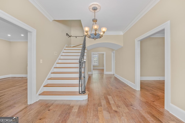 stairs with crown molding, wood-type flooring, and a notable chandelier