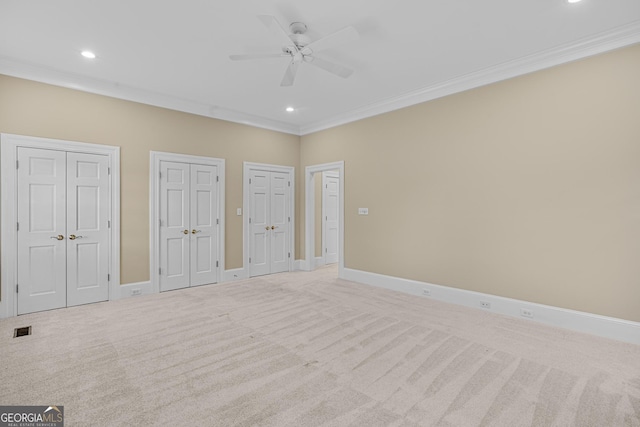 unfurnished bedroom featuring multiple closets, ornamental molding, light carpet, and ceiling fan