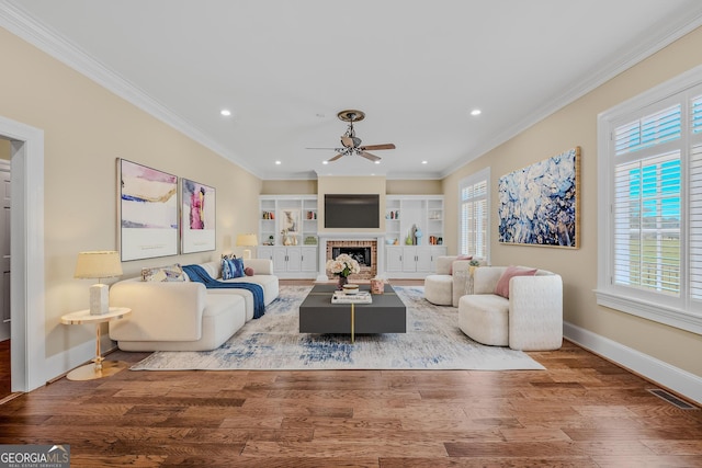 living room with crown molding, hardwood / wood-style flooring, built in features, ceiling fan, and a fireplace