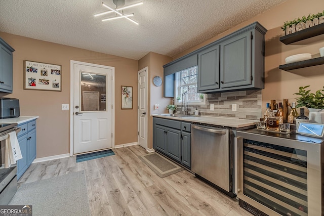 kitchen with sink, light hardwood / wood-style flooring, appliances with stainless steel finishes, beverage cooler, and backsplash