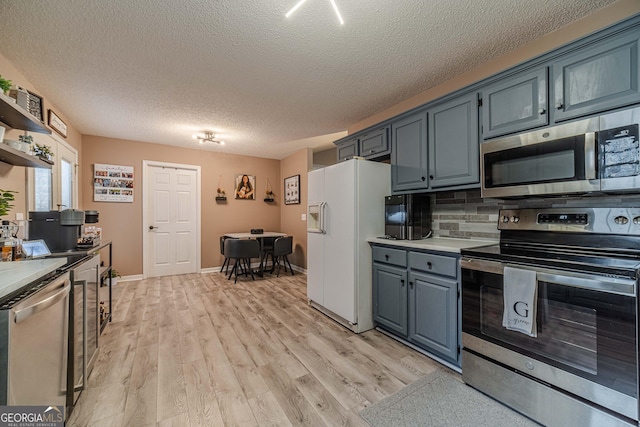 kitchen featuring light hardwood / wood-style flooring, blue cabinetry, backsplash, stainless steel appliances, and a textured ceiling