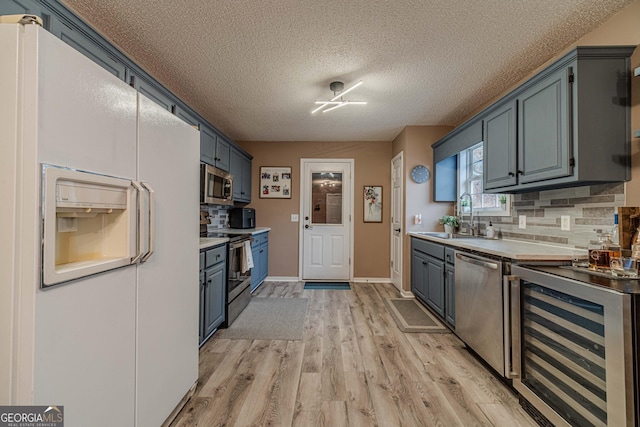 kitchen featuring appliances with stainless steel finishes, sink, wine cooler, decorative backsplash, and light hardwood / wood-style flooring