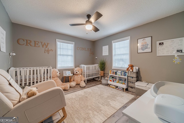 bedroom featuring multiple windows, ceiling fan, a crib, and light hardwood / wood-style floors