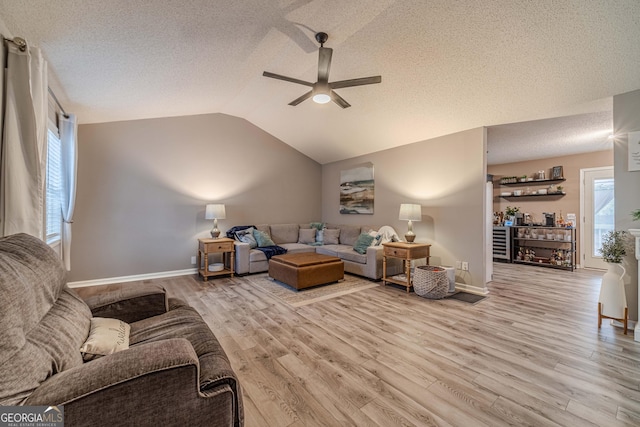 living room with ceiling fan, lofted ceiling, a textured ceiling, and light wood-type flooring