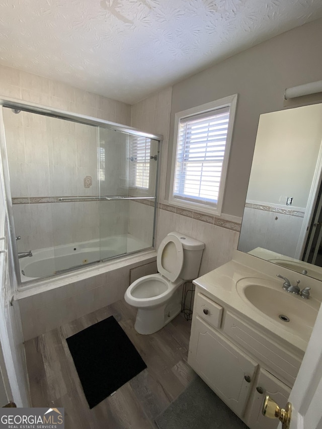 full bathroom featuring toilet, a textured ceiling, tile walls, vanity, and enclosed tub / shower combo