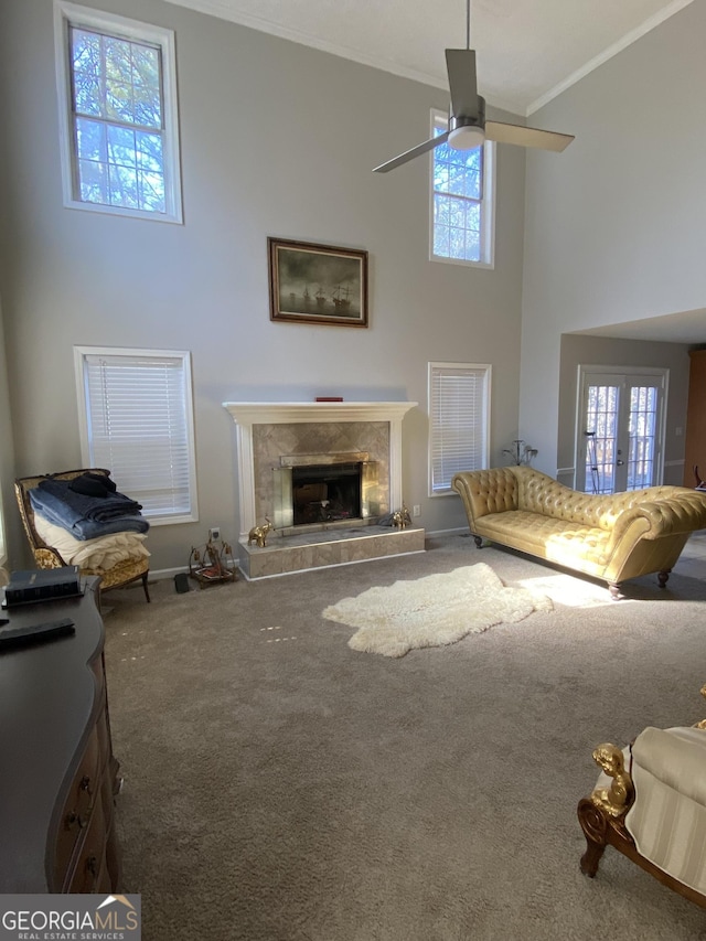 carpeted living room with ornamental molding, a towering ceiling, ceiling fan, and a fireplace