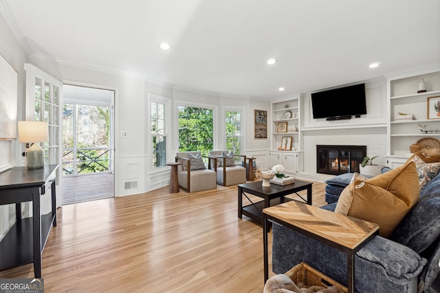 living room featuring built in shelves, plenty of natural light, a fireplace, and light hardwood / wood-style floors