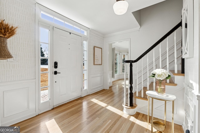 entryway featuring plenty of natural light, ornamental molding, and light wood-type flooring