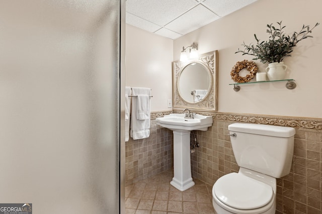 bathroom featuring a drop ceiling, tile patterned flooring, tile walls, and toilet