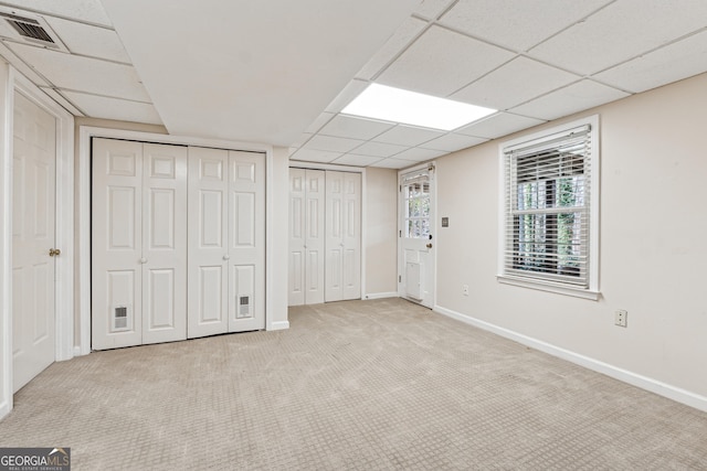 basement with a paneled ceiling and light carpet