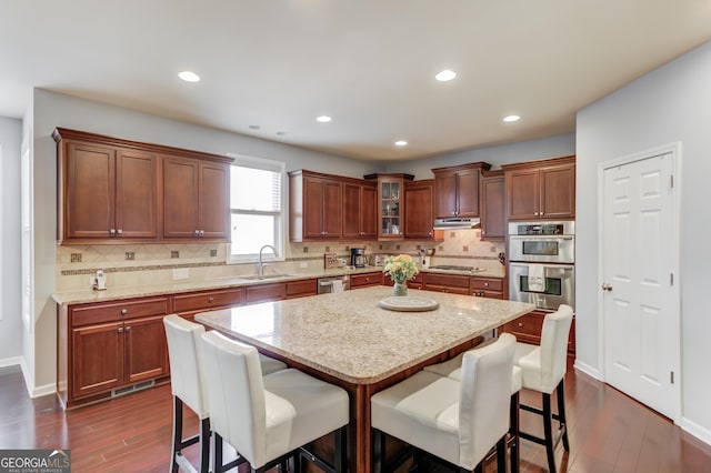 kitchen featuring stainless steel appliances, a center island, sink, and light stone countertops