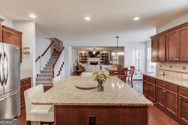 kitchen featuring hanging light fixtures, stainless steel refrigerator, a kitchen breakfast bar, a kitchen island, and light stone countertops