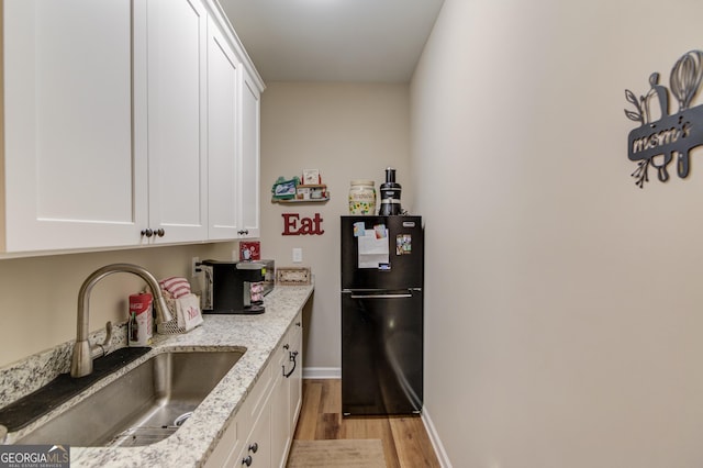 kitchen featuring white cabinetry, sink, light stone counters, and black fridge