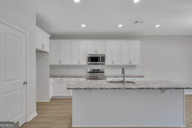 kitchen featuring sink, appliances with stainless steel finishes, an island with sink, light stone countertops, and white cabinets