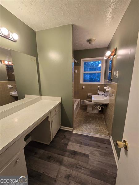 full bathroom with toilet, tiled shower / bath, a textured ceiling, vanity, and hardwood / wood-style flooring