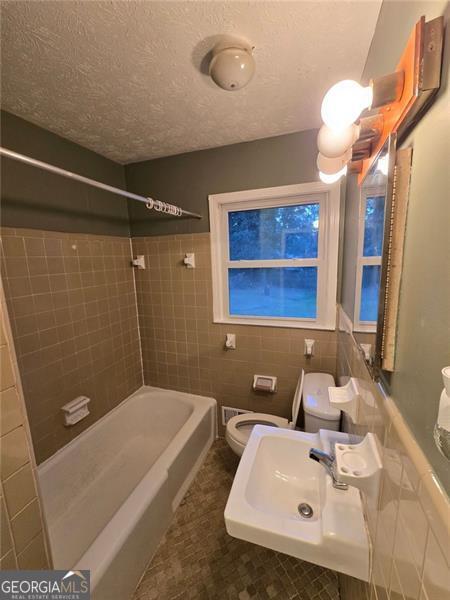 full bathroom with tiled shower / bath, sink, tile walls, toilet, and a textured ceiling