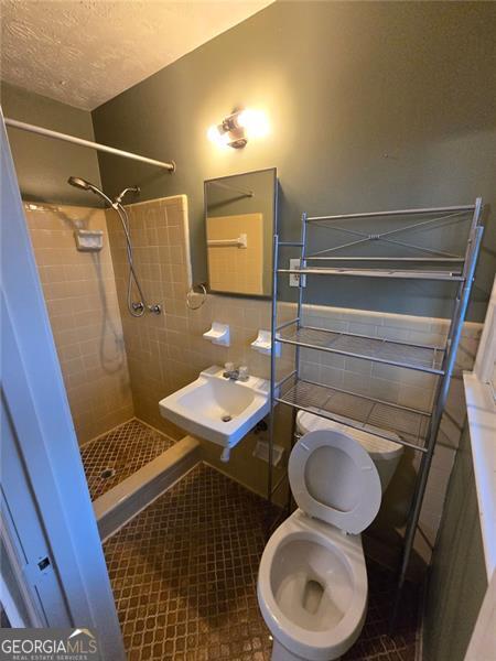 bathroom featuring sink, tile patterned flooring, tiled shower, toilet, and a textured ceiling