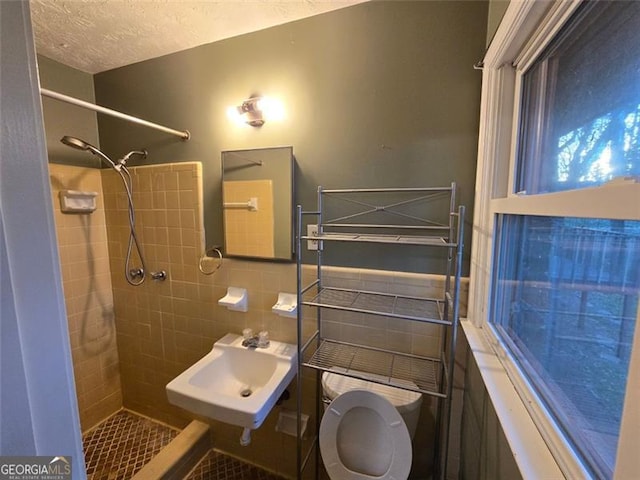 bathroom featuring sink, tile walls, tiled shower, toilet, and a textured ceiling