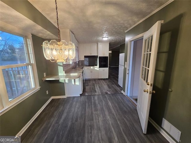 kitchen featuring dark wood-type flooring, white cabinetry, crown molding, a notable chandelier, and pendant lighting