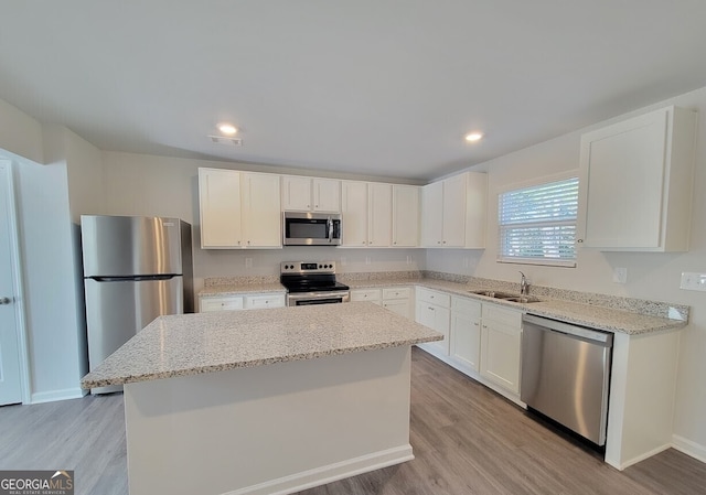 kitchen featuring light hardwood / wood-style flooring, appliances with stainless steel finishes, light stone countertops, white cabinets, and a kitchen island