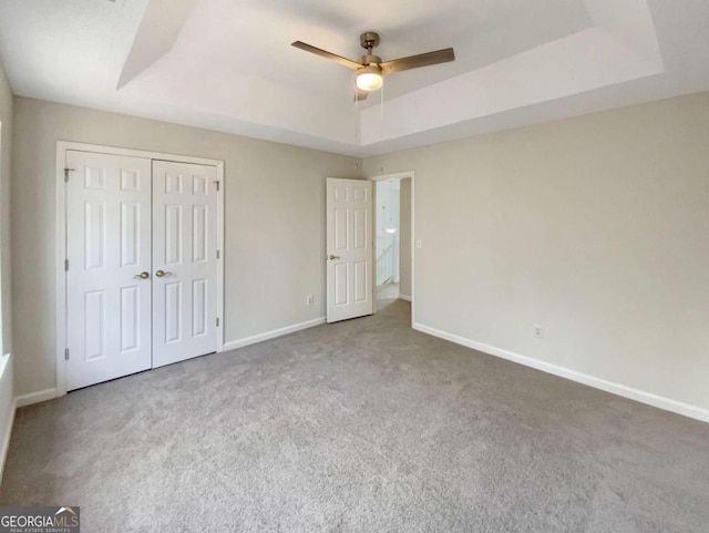 unfurnished bedroom featuring a raised ceiling, carpet floors, ceiling fan, and a closet