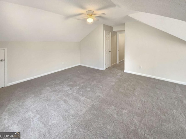 additional living space featuring vaulted ceiling, dark carpet, a textured ceiling, and ceiling fan