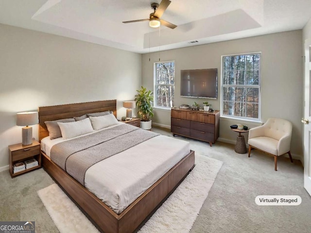 carpeted bedroom with ceiling fan and a tray ceiling